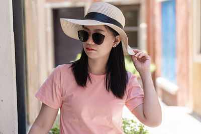 Portrait of young woman wearing sunglasses standing against pink wall