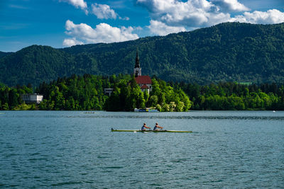 People boating on lake bled against church and tree mountain