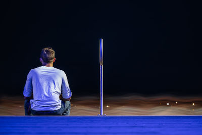 Rear view of man standing against illuminated wall at night