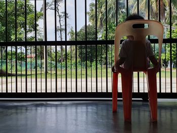 Rear view of man standing by railing against window