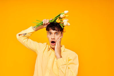 Portrait of young man holding flowers against yellow background