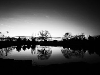 Reflection of silhouette trees in lake against sky