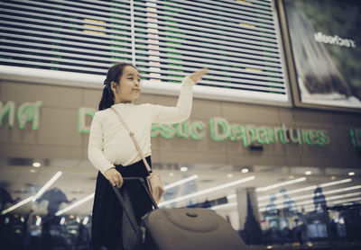 Low angle view of girl with luggage standing in airport