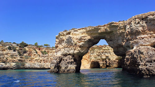 Rock formation by sea against clear blue sky