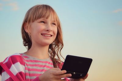 Portrait of smiling woman using mobile phone against sky