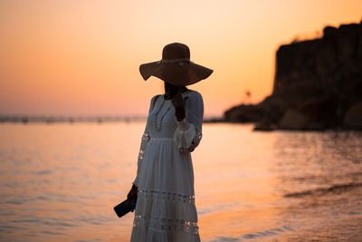 Beautiful african woman in sun hat walks on beach at sunset. calming coral color, design of 2022