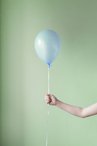 Cropped hand of person holding balloon against green wall
