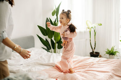 A charming little girl plays with dolls with her mom on the bed during the day. motherhood, caring.