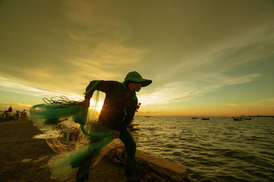 Fisherman throwing net in sea against sky during sunset