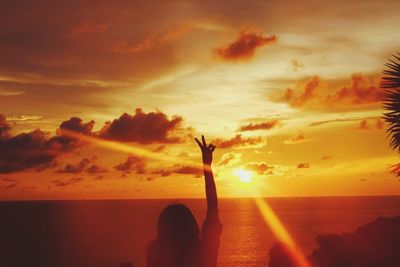 Rear view of silhouette woman gesturing peace sign at beach against sky during sunset