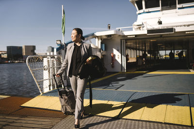 Businesswoman pulling wheeled luggage while disembarking from ferry on sunny day