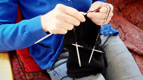 Midsection of woman knitting hat at home