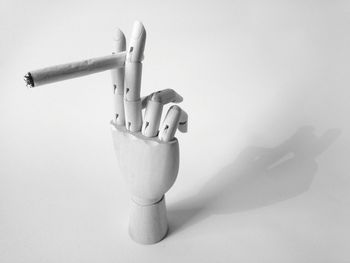 Close-up of figurine hand holding cigarette over white background