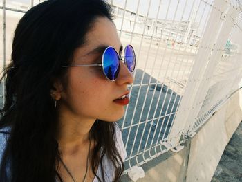 Close-up of young woman leaning on fence while wearing sunglasses