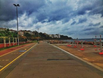 Empty road in city against cloudy sky