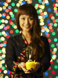 Portrait of woman with oil lamp against illuminated lights