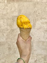 Hand holding ice cream cone against wall