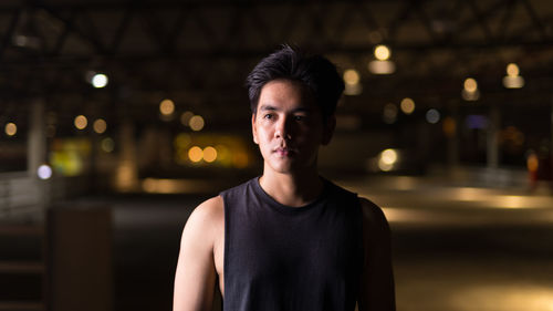 Portrait of young man standing against illuminated city at night