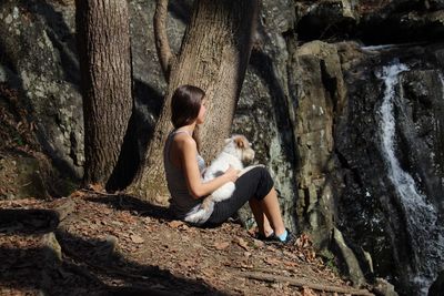High angle view of woman sitting with dog by trees at forest