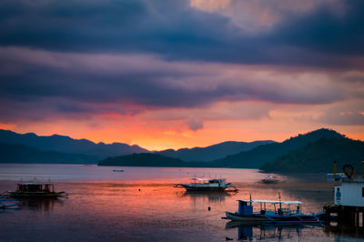 Sailboats moored on sea against sky during sunset