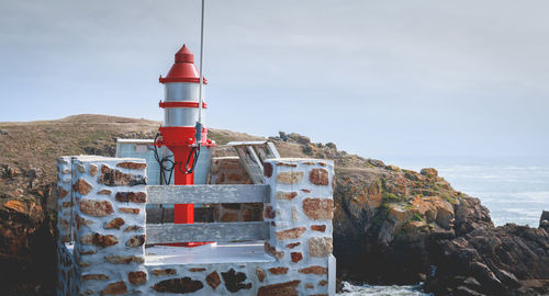 Lighthouse on rock by sea against sky