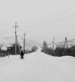 Rear view full length of person walking on snow covered road