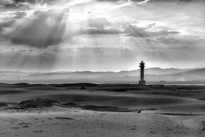 Lighthouse on landscape against cloudy sky