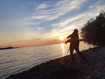 Silhouette man standing on beach against sky during sunset