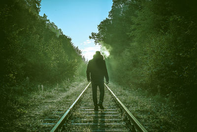 Rear view of man walking on railroad track