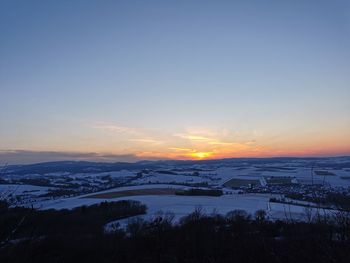 Snow covered landscape against sky during sunset