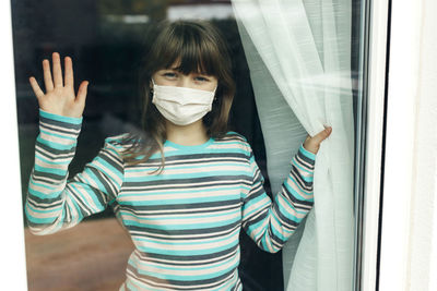 Sad teenage girl in a mask looks through the window. the introduction of quarantine