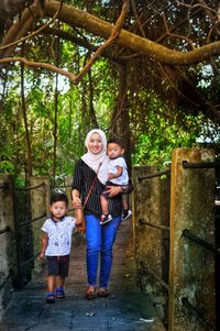 Portrait of mother with cute sons walking on footpath against trees