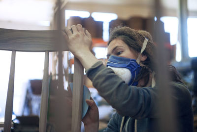 Carpenter rubbing paper on wooden chair at workshop