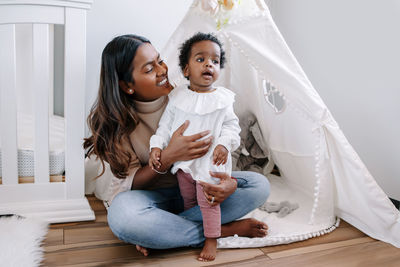 Happy smiling young indian mother playing with black baby girl daughter. family mixed race people. 