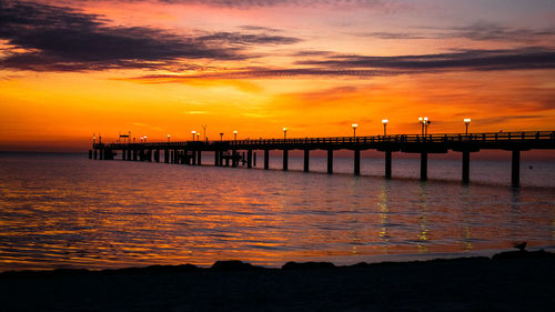 Silhouette pier on sea against orange sky