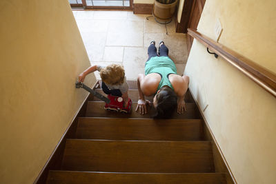 High angle view of mother practicing push-ups while son playing with toy crane on wooden steps at home