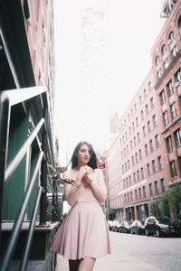 Portrait of young woman standing against buildings in city