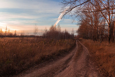 Dirt road amidst field against sky during sunset