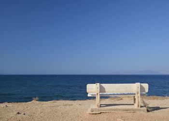 Chair on beach against clear blue sky