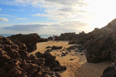 Rocks on beach against sky during sunset