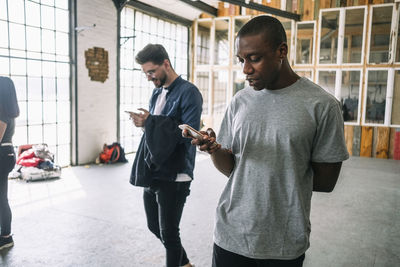 Confident young businessman using smart phone while walking by colleague at creative workplace