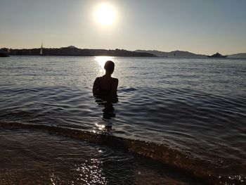 Man sitting in sea against sky during sunset