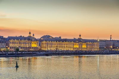 River in city against sky during sunset