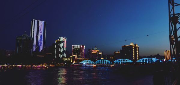 Illuminated city by river against sky at night
