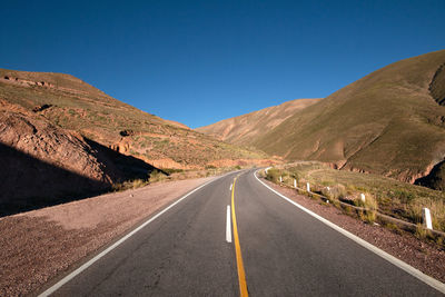 Empty road along landscape and mountains against clear blue sky