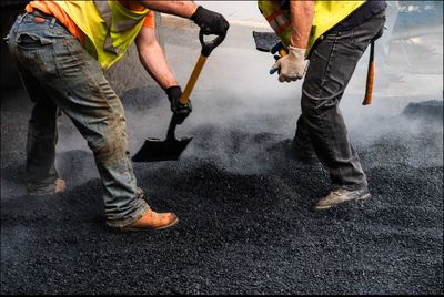 Low section of manual workers using spade on gravel