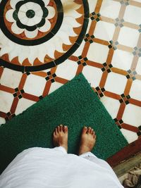 Low section of man standing on green doormat at home