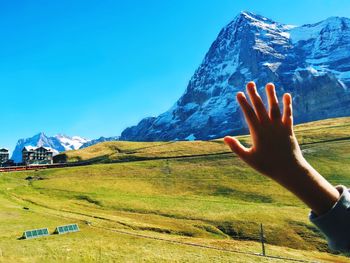 Cropped image of hand by snowcapped mountain against sky