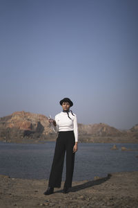 Long shot of an indian girl standing near a lake surrounded with mountains, wearing white top 