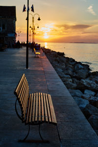 Deck chairs on beach against sky during sunset